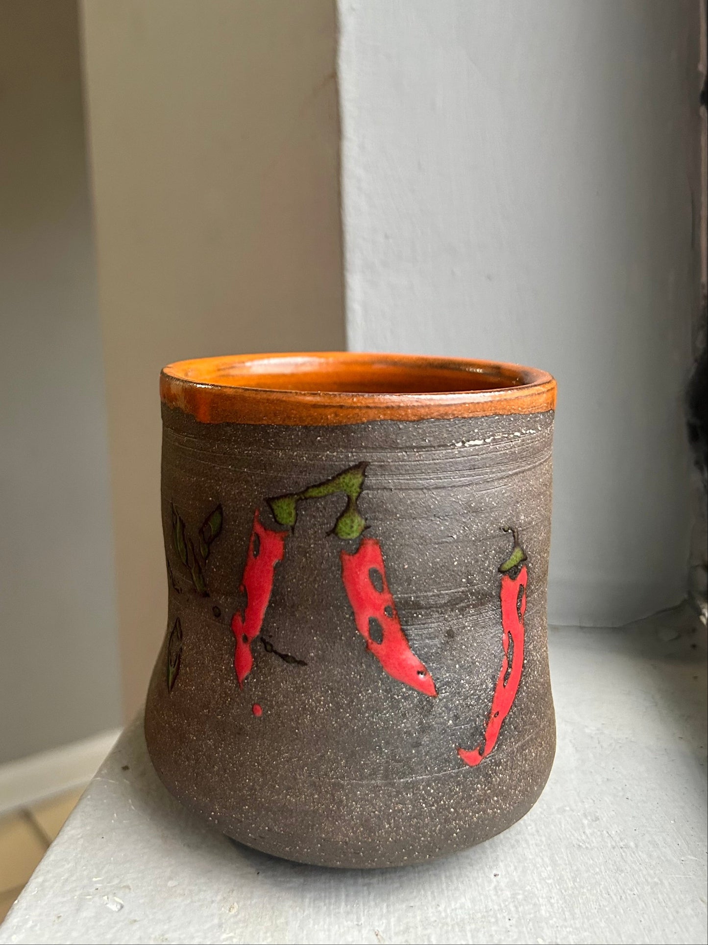 Ceramic cup with red chili pepper design on a white surface